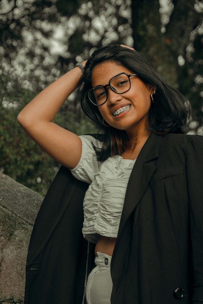 Portrait of a woman outdoors, wearing glasses and smiling with a forest background.