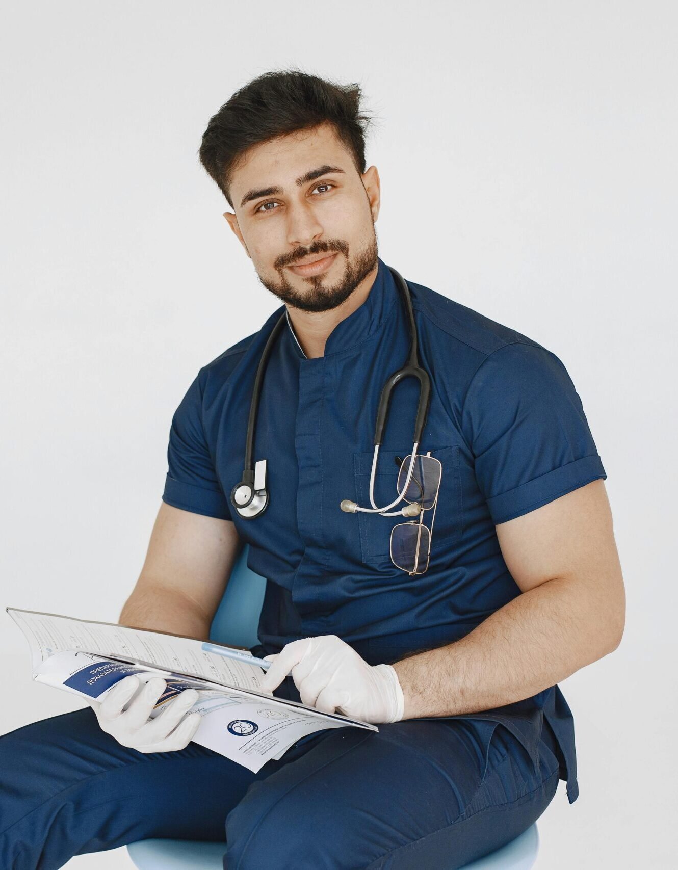 Young male doctor in blue scrubs reviewing medical records with a confident smile.
