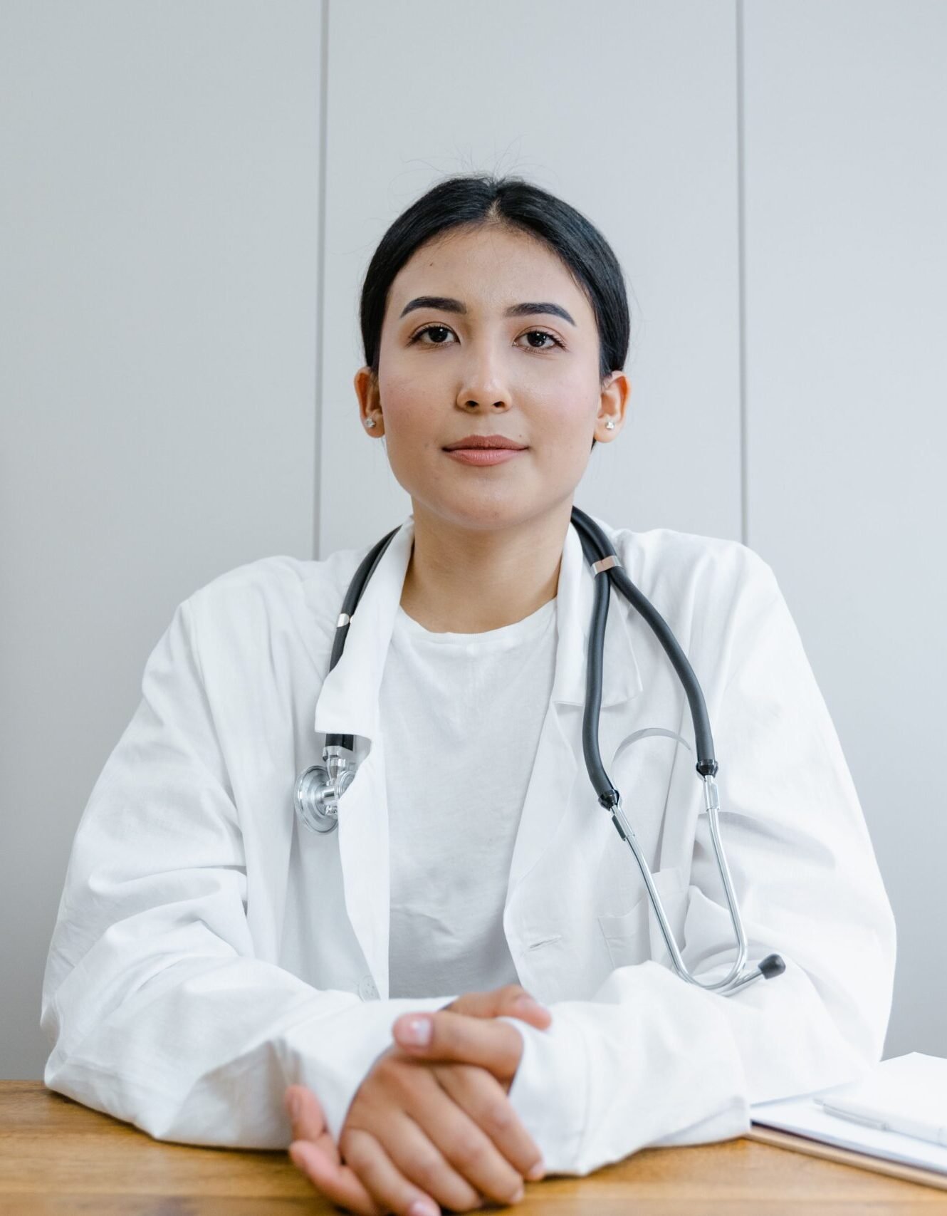 Young female doctor sitting at desk with stethoscope, ready for telehealth consultation.